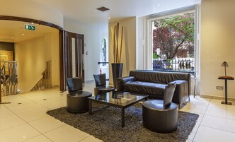A modern lobby with a leather sofa, glass coffee table, and black chairs. There is a large window with a view of trees and a street.