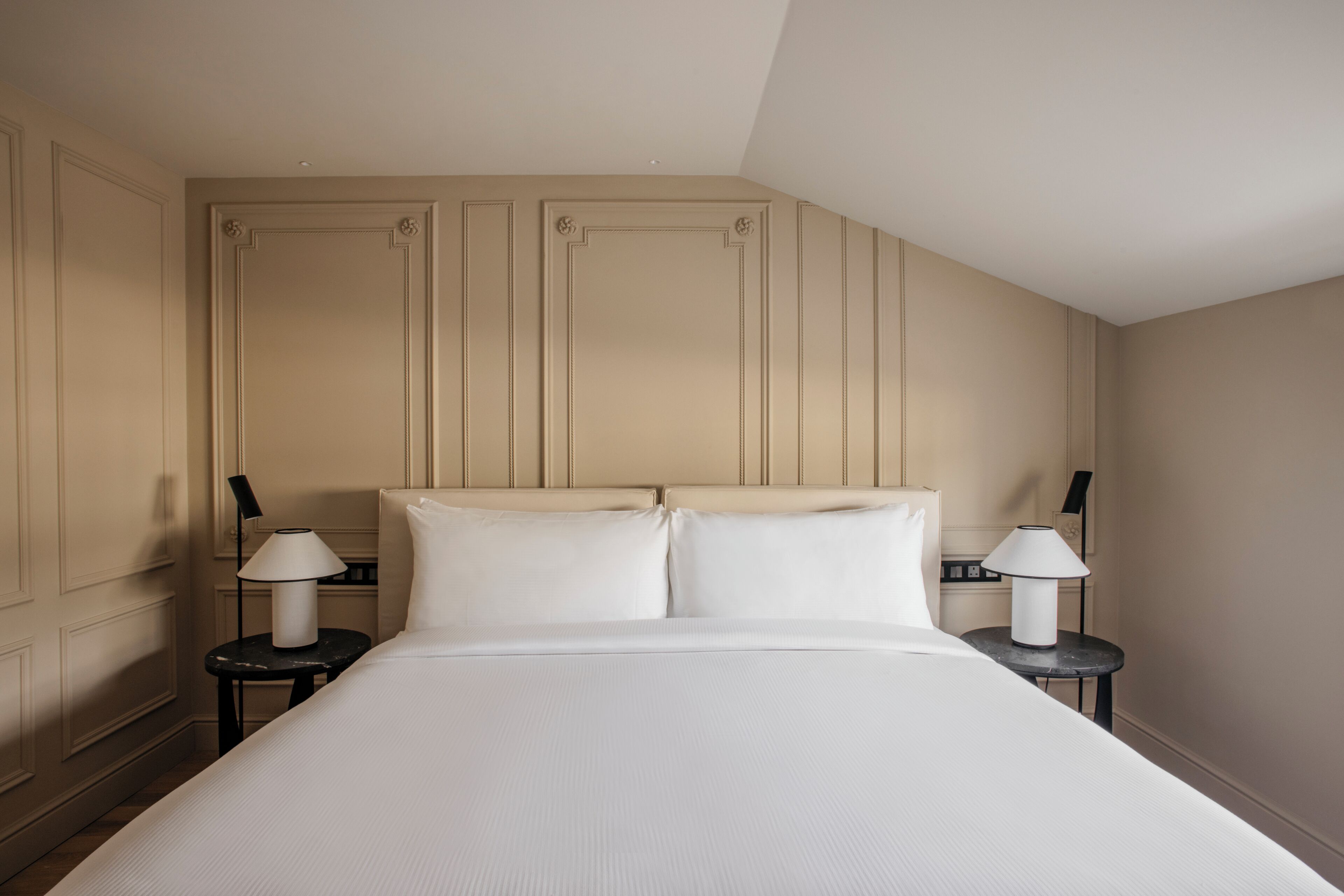 A neatly made bed with two pillows and two bedside tables with lamps, set against a wall with paneling.