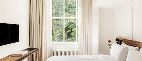 A hotel room with a large bed, a bedside table with a book, a TV, and a window with curtains.