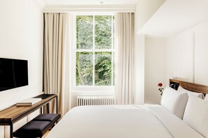 Camera d'albergo con un letto grande, un comodino con un libro, una TV e una finestra con tende.