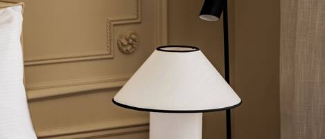 A neatly made bed with white linens, a black floor lamp with a white shade, and a small black table beside it.