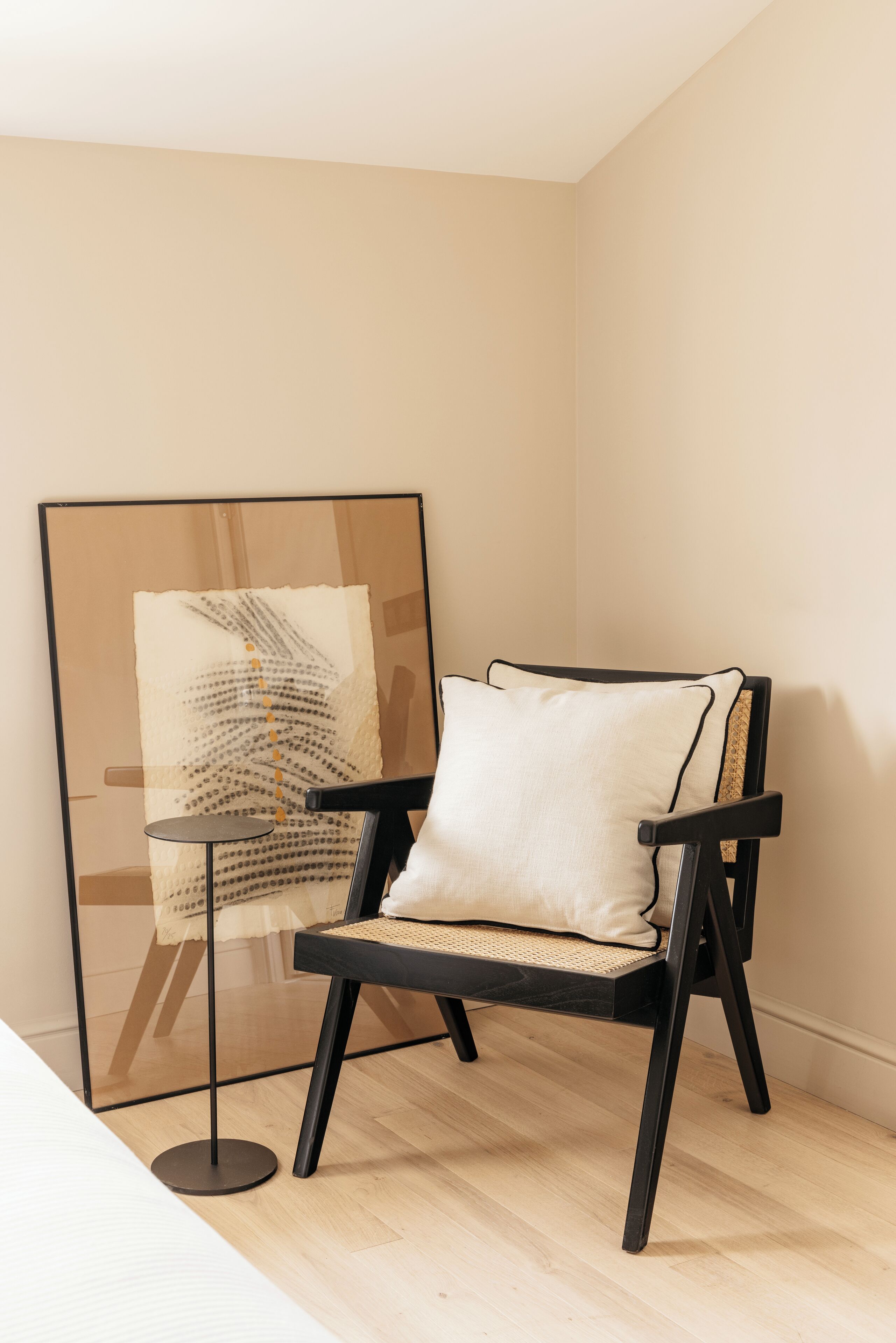 A modern chair with a woven seat and black frame, positioned next to a framed artwork on a glass stand.