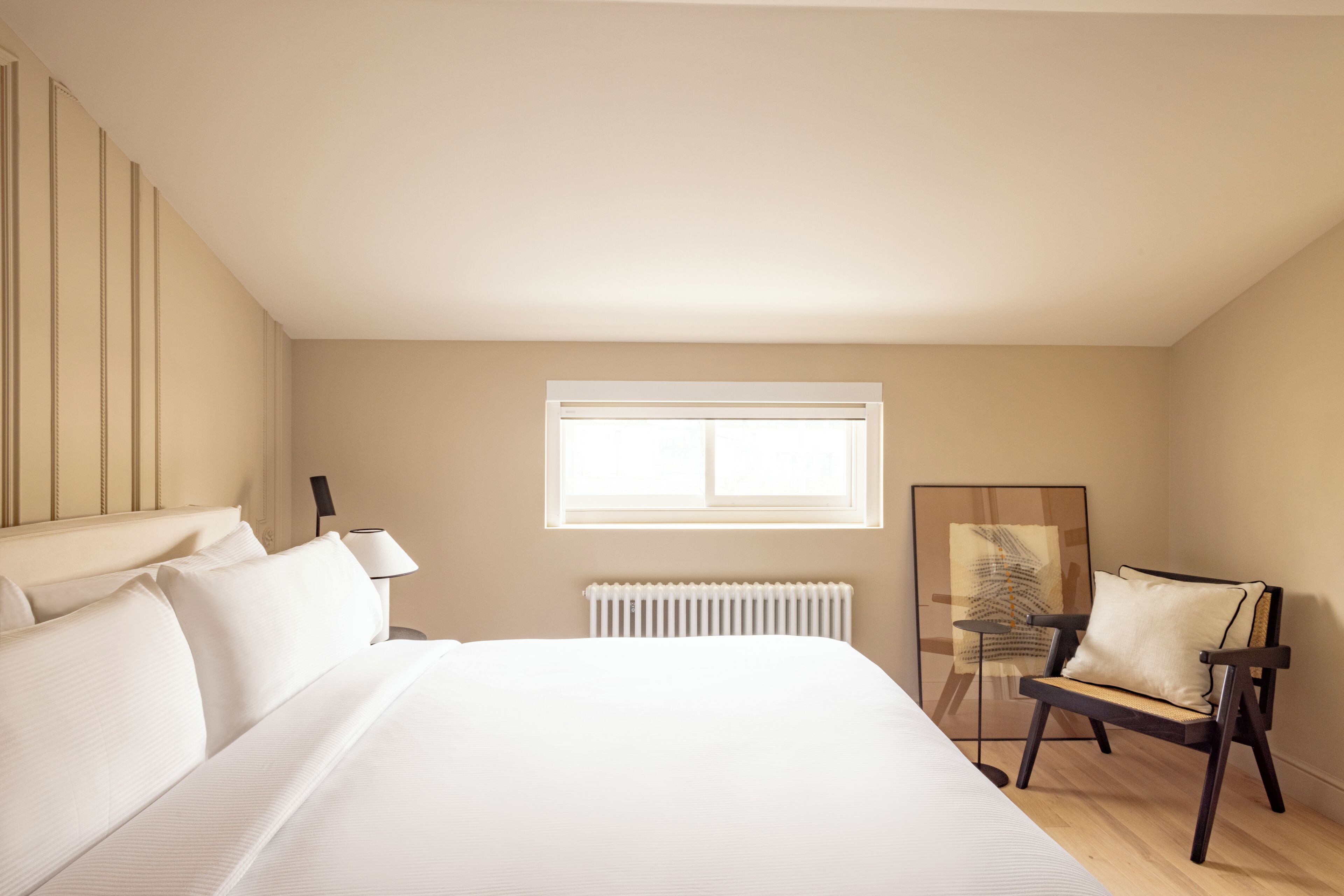 A bedroom with a large bed, a chair, a radiator, and a window.