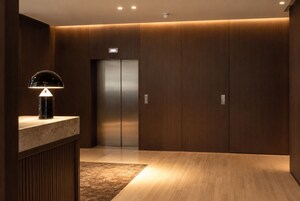 Um elevador moderno com visor digital, balcão de mármore com luminária e painéis de madeira.