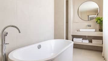 Un baño moderno con una bañera independiente, un espejo redondo y un lavabo empotrado con un perchero.