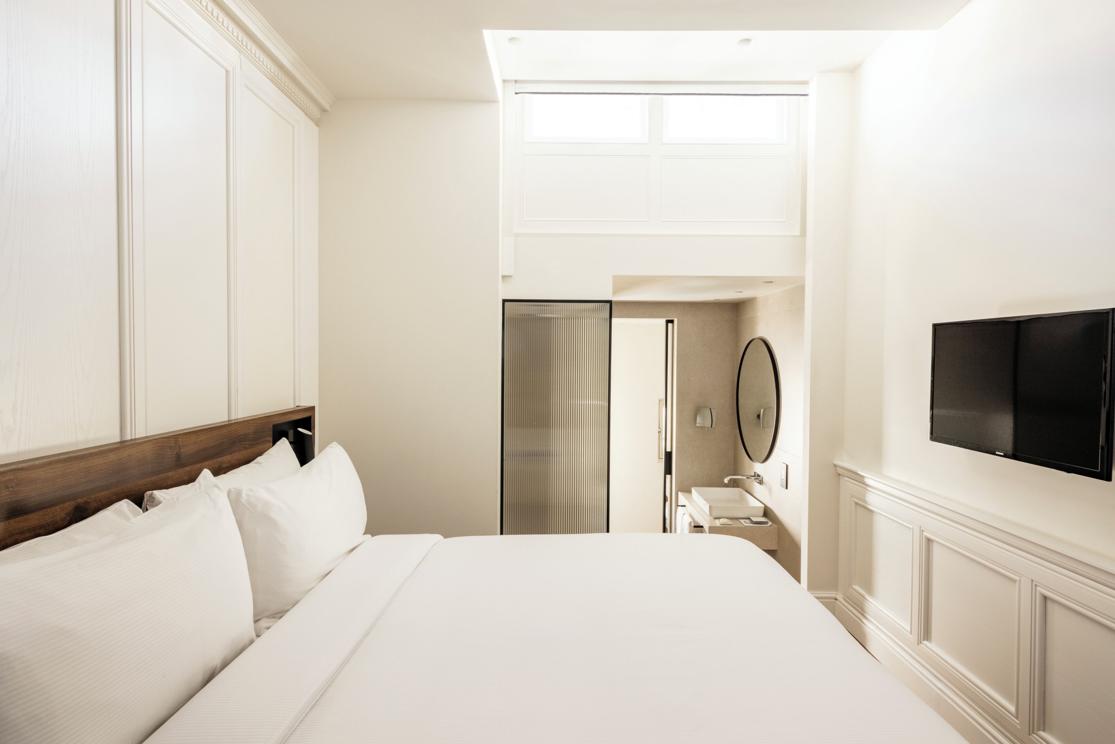 Une chambre d’hôtel avec un grand lit, un téléviseur fixé au mur et une salle de bain visible à travers une porte ouverte.