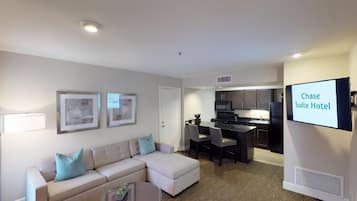 A modern hotel room with a living area, kitchenette, and a television displaying 'Chase Suite Hotel'.