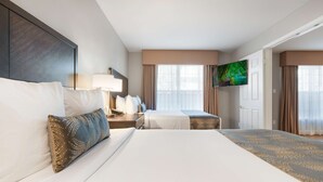 A hotel room with two beds, a TV, a desk with a lamp, and a large window with curtains. - Chase Suites Hotel Brea-Fullerton (Brea)