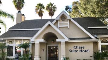 The exterior of the Chase Suite Hotel with a prominent entrance, a covered patio area, and a parking lot in front.