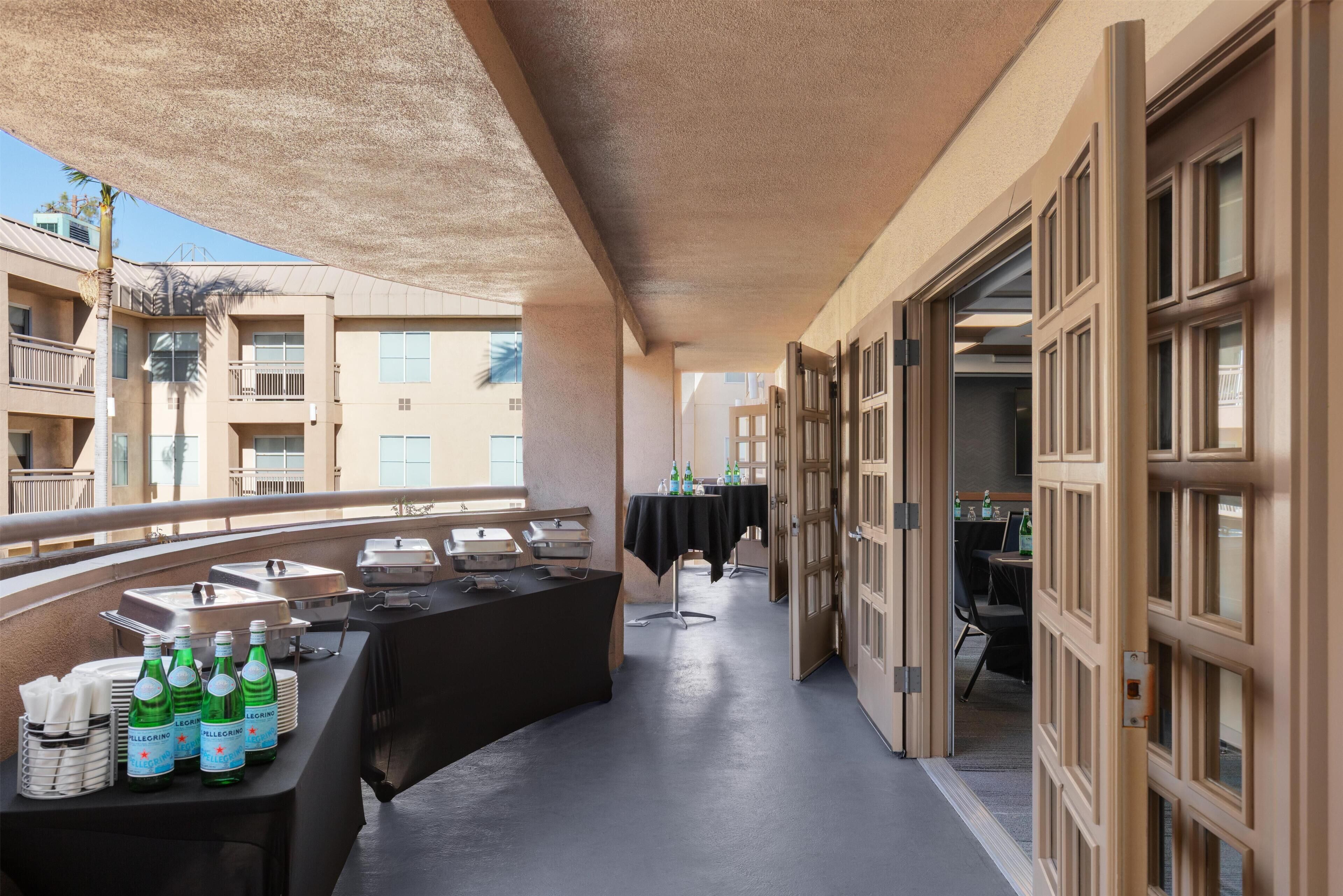 Un balcon avec une table dressée pour un repas, des bouteilles d’eau Pellegrino et une vue sur la façade de l’immeuble.