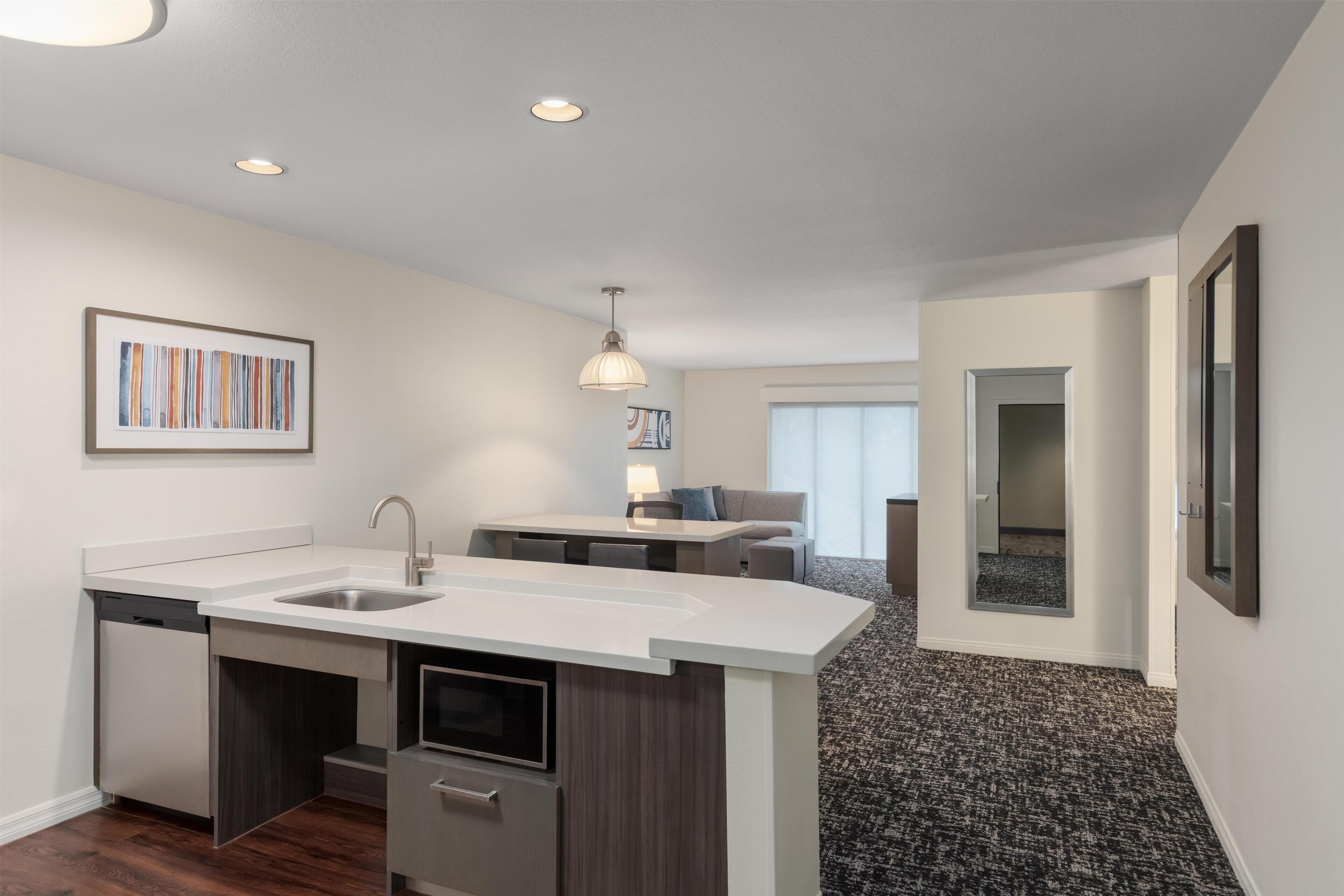 Una cocina moderna con lavavajillas incorporado, un comedor con mesa y sillas, y una sala de estar con sofá y lámpara.