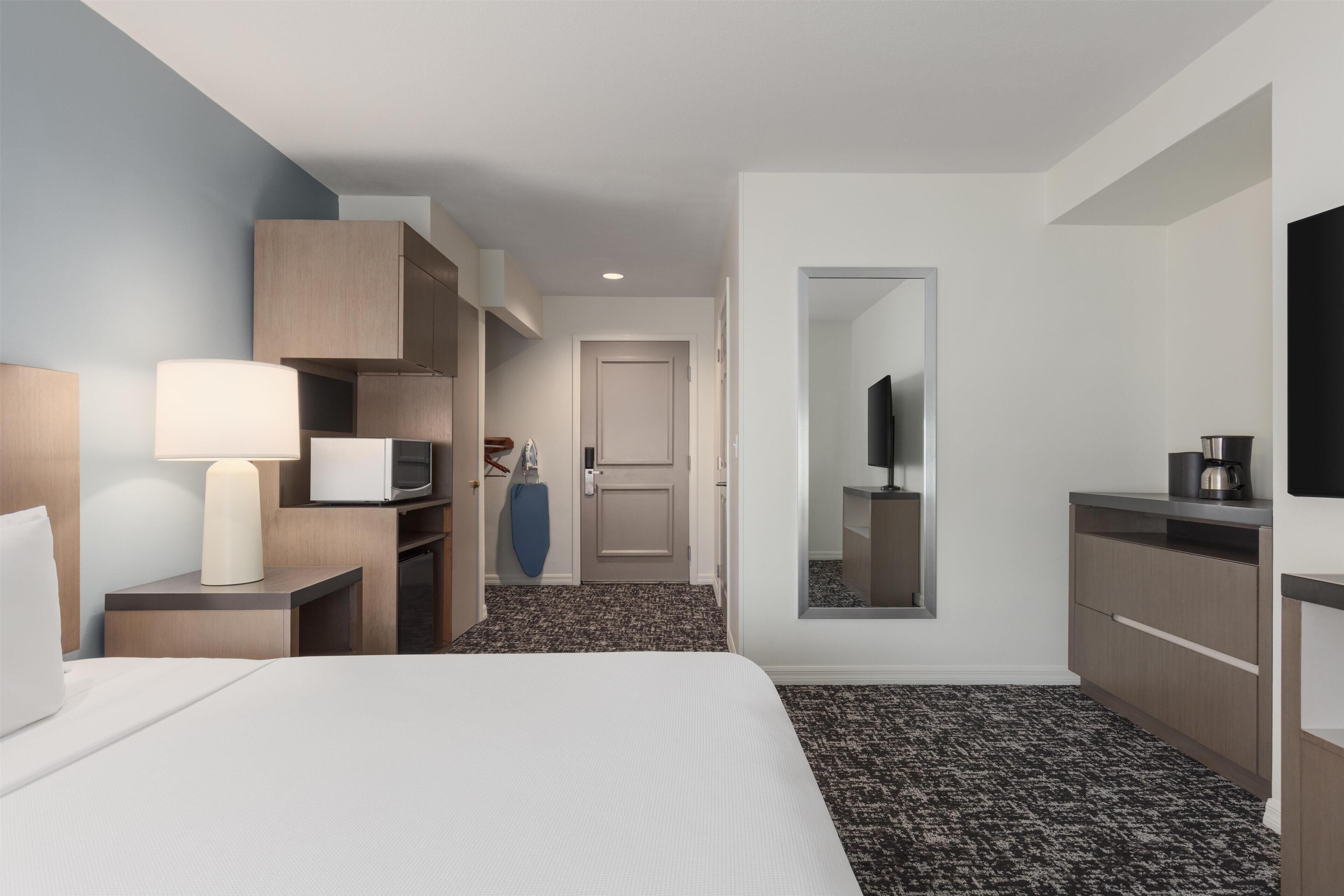 A hotel room with a bed, a desk with a lamp, a wardrobe, a television, and a coffee machine.