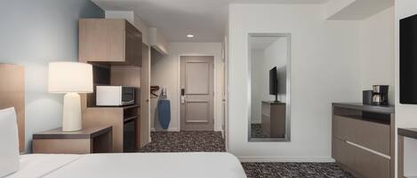 A hotel room with a bed, a desk with a lamp, a wardrobe, a television, and a coffee machine.