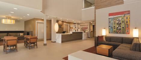 A spacious lobby with a reception desk, seating area, and a modern kitchen in the background.