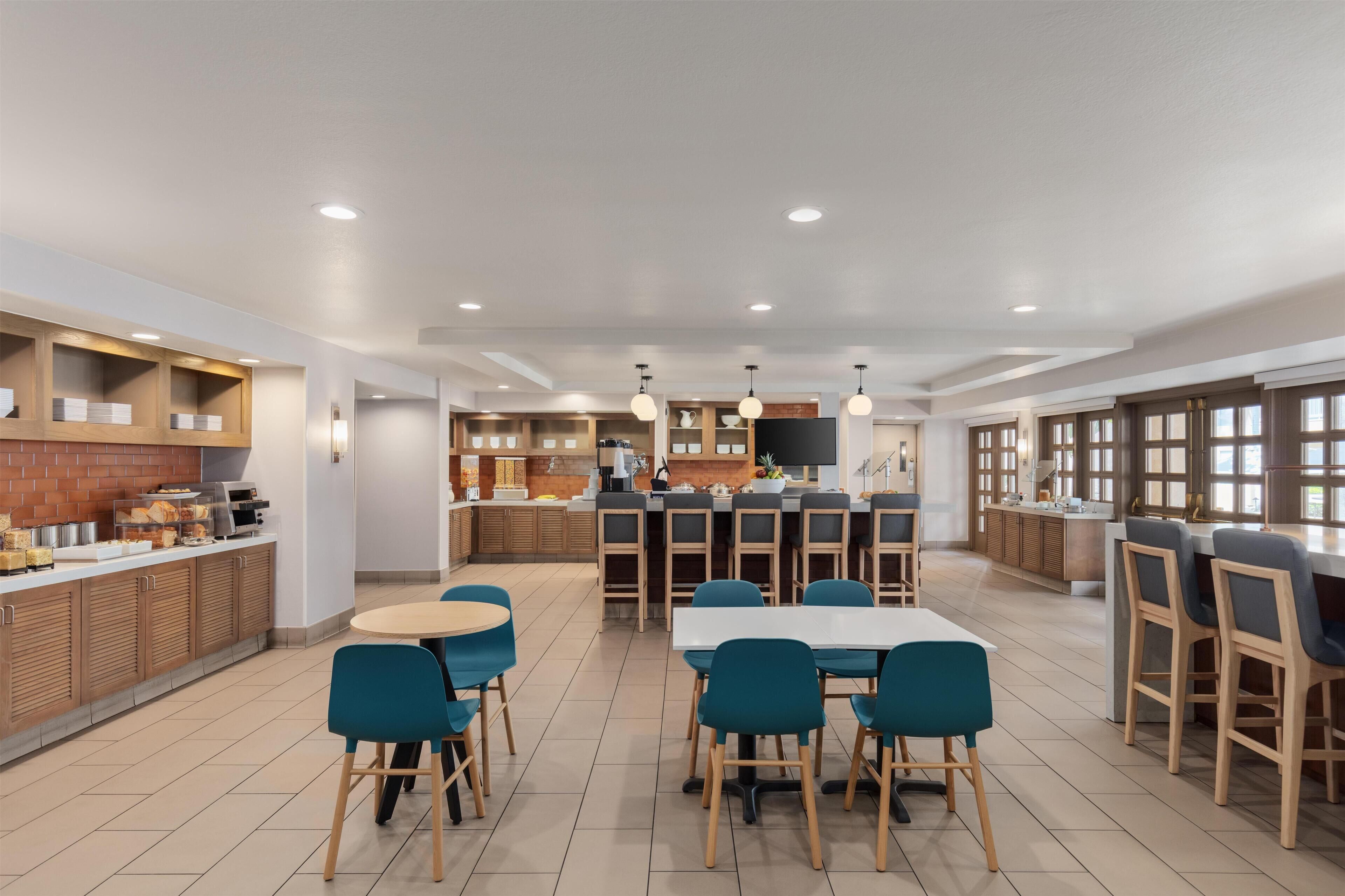A modern kitchen with a central island, bar seating, and a dining area with round tables and chairs.