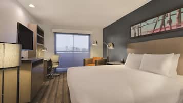 A hotel room with a large bed, a desk with a computer, a chair, a TV, and a window with a view.