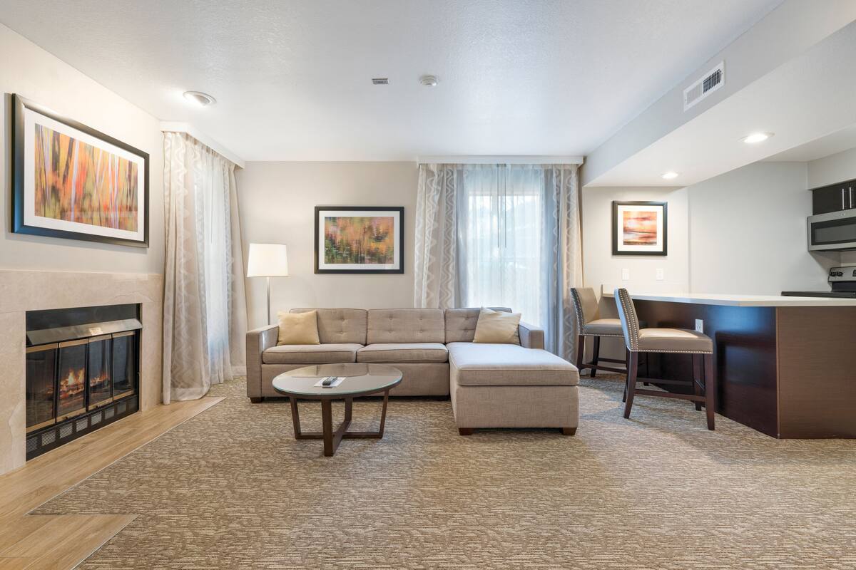 A modern living room with a fireplace, a sectional sofa, a coffee table, and a dining area with chairs and a kitchen counter.