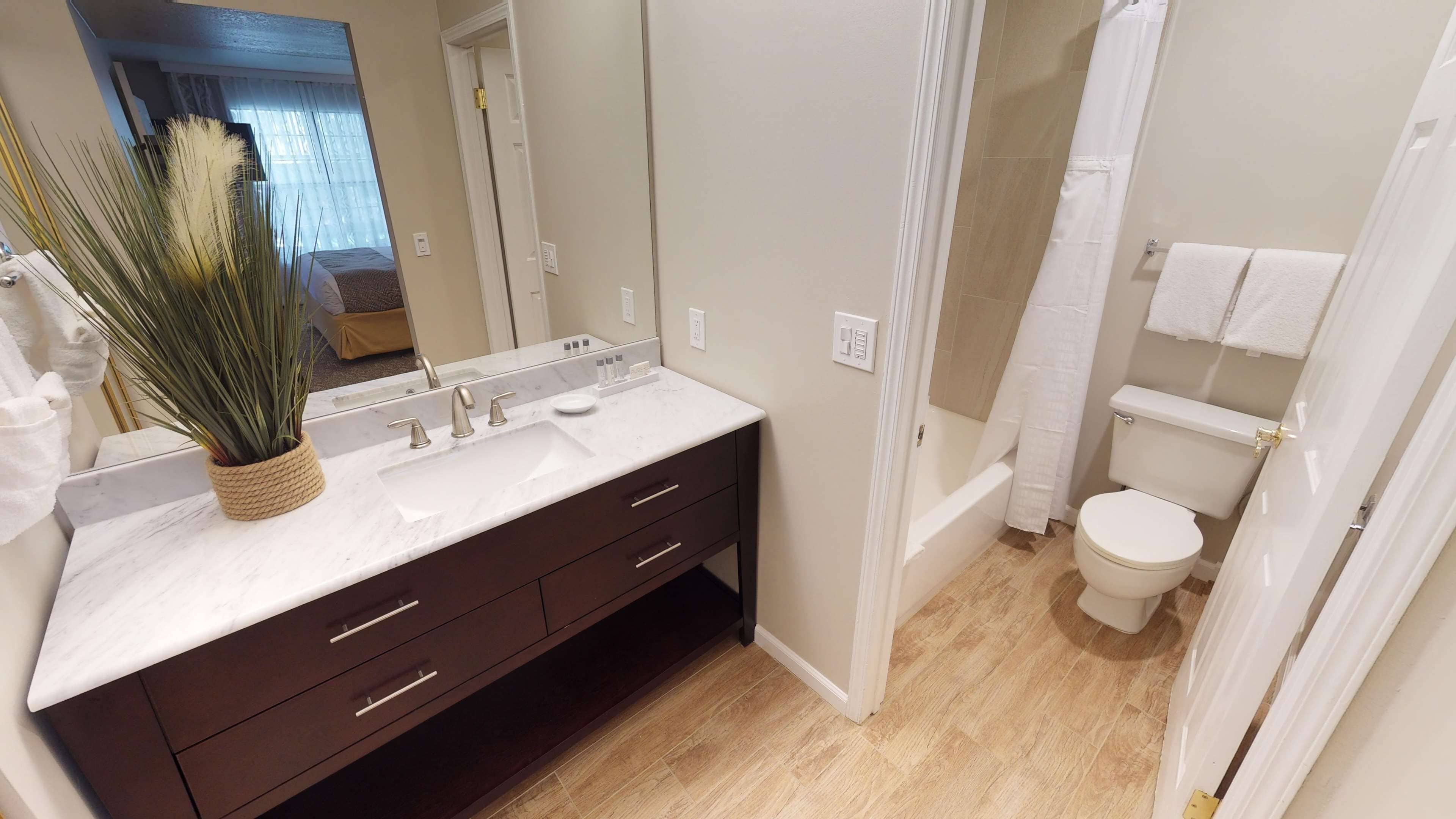 A bathroom with a marble sink, dark wooden cabinet, white toilet, and a shower curtain.