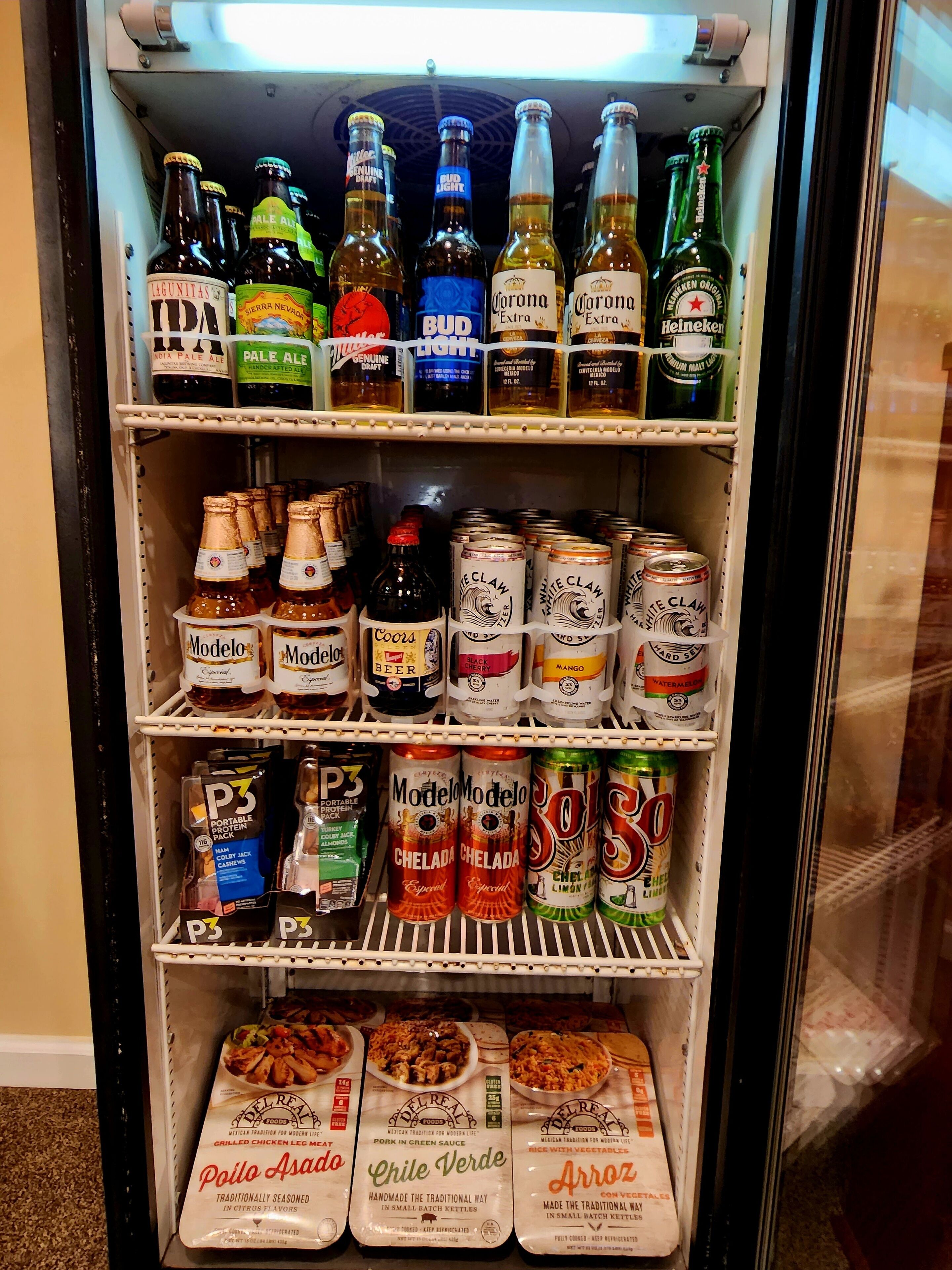A beverage refrigerator stocked with various beers, canned drinks, and protein packs.