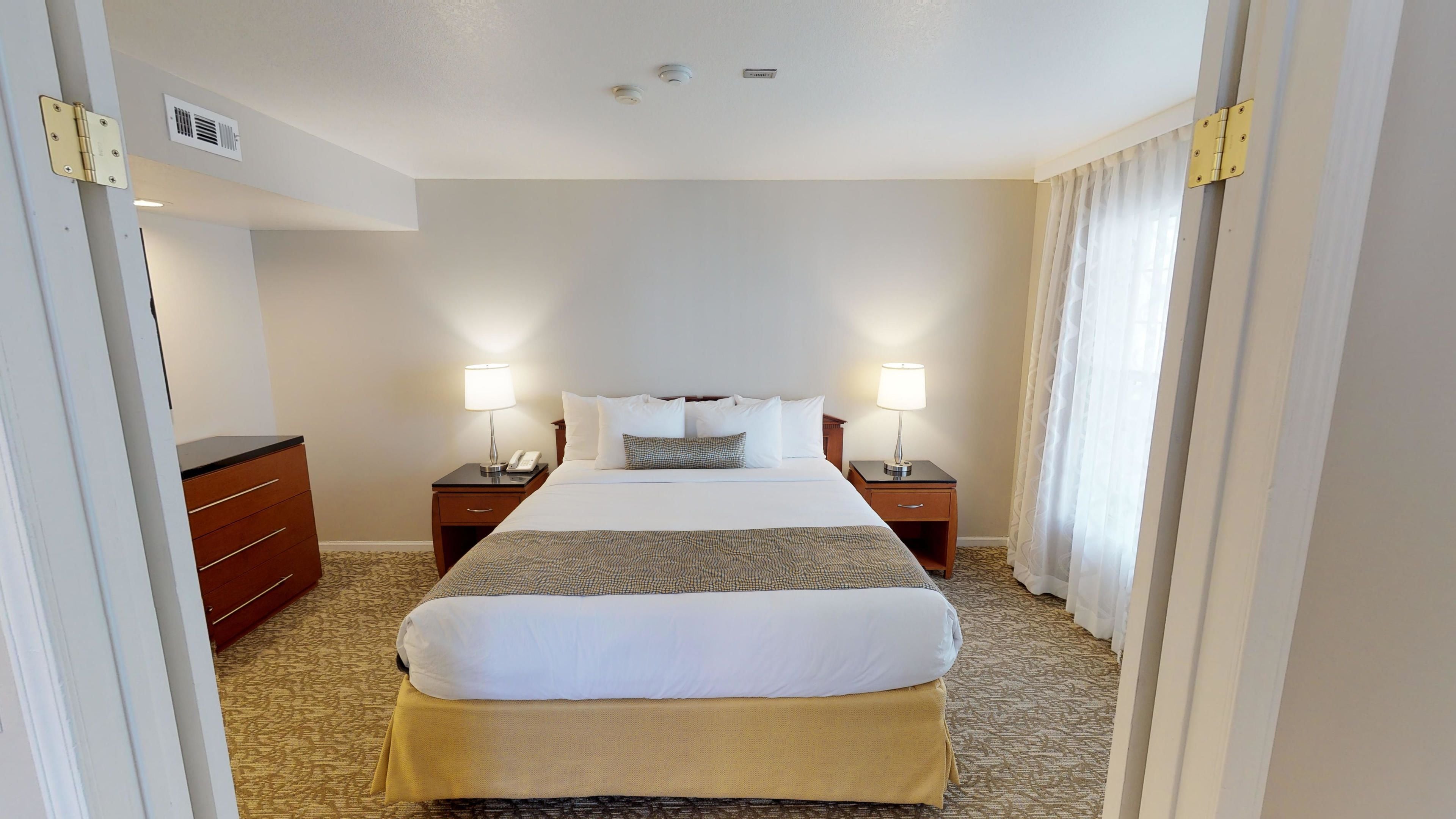 A hotel room with a large bed, two bedside tables with lamps, a telephone, and a wardrobe.