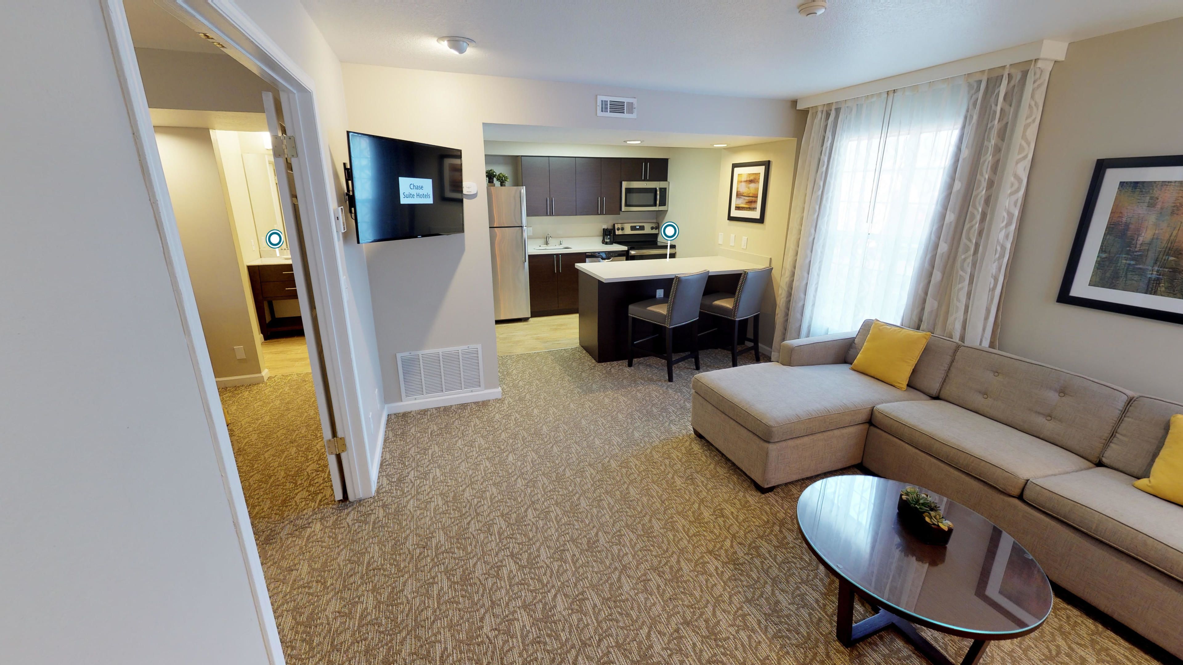 A modern hotel room with a living area, kitchenette, and a dining area.