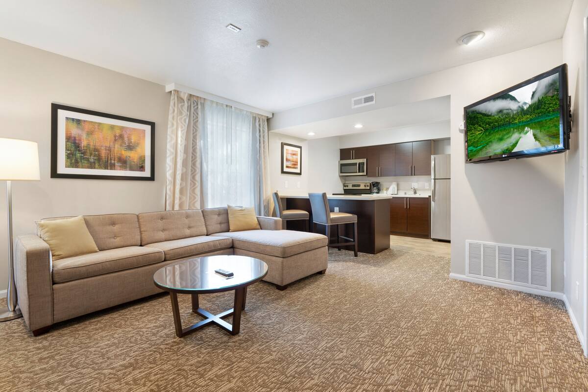 A modern hotel room with a living area, kitchenette, and a large TV.