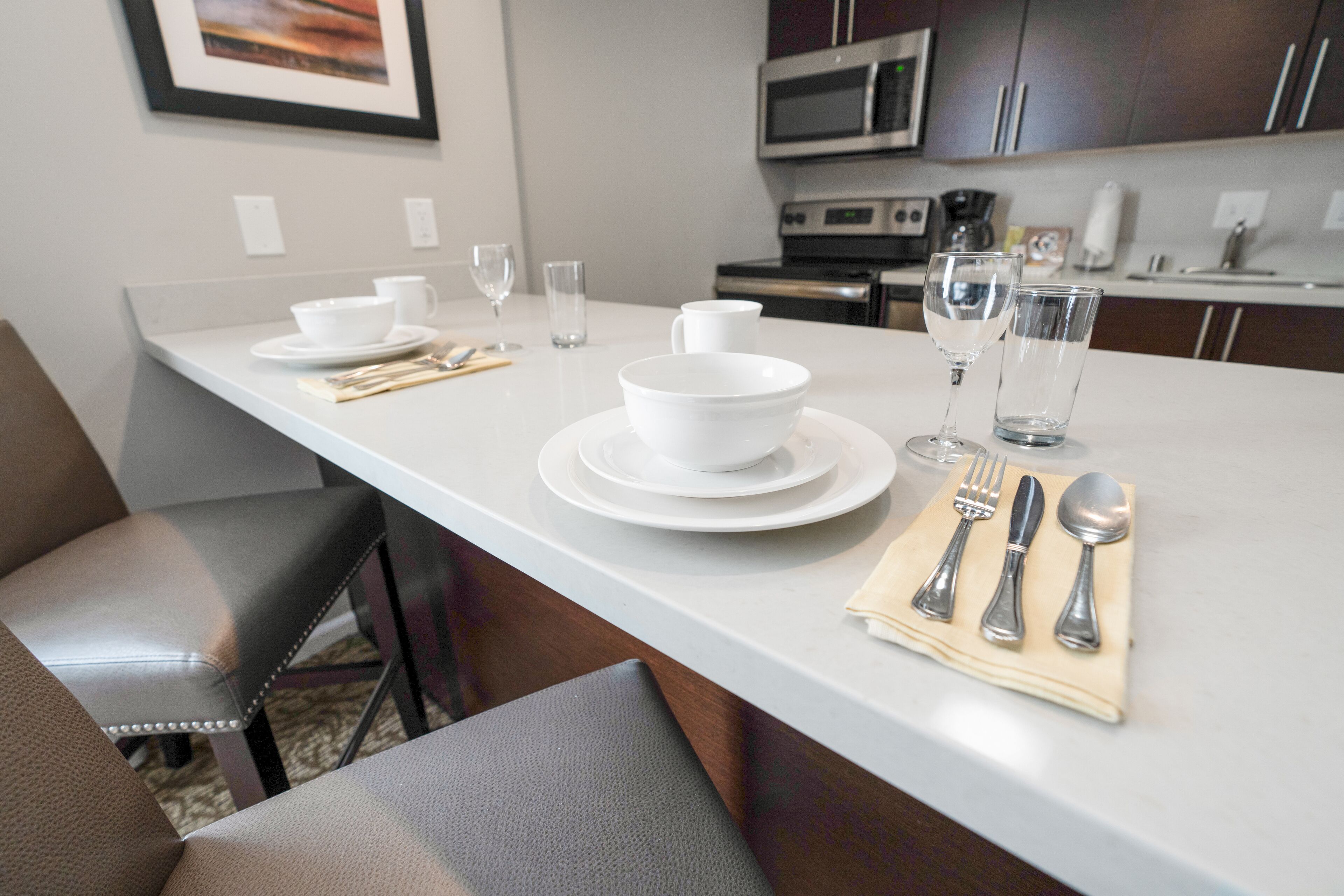 A modern kitchen with white countertops, stainless steel appliances, and a dining area set with white tableware and glasses.