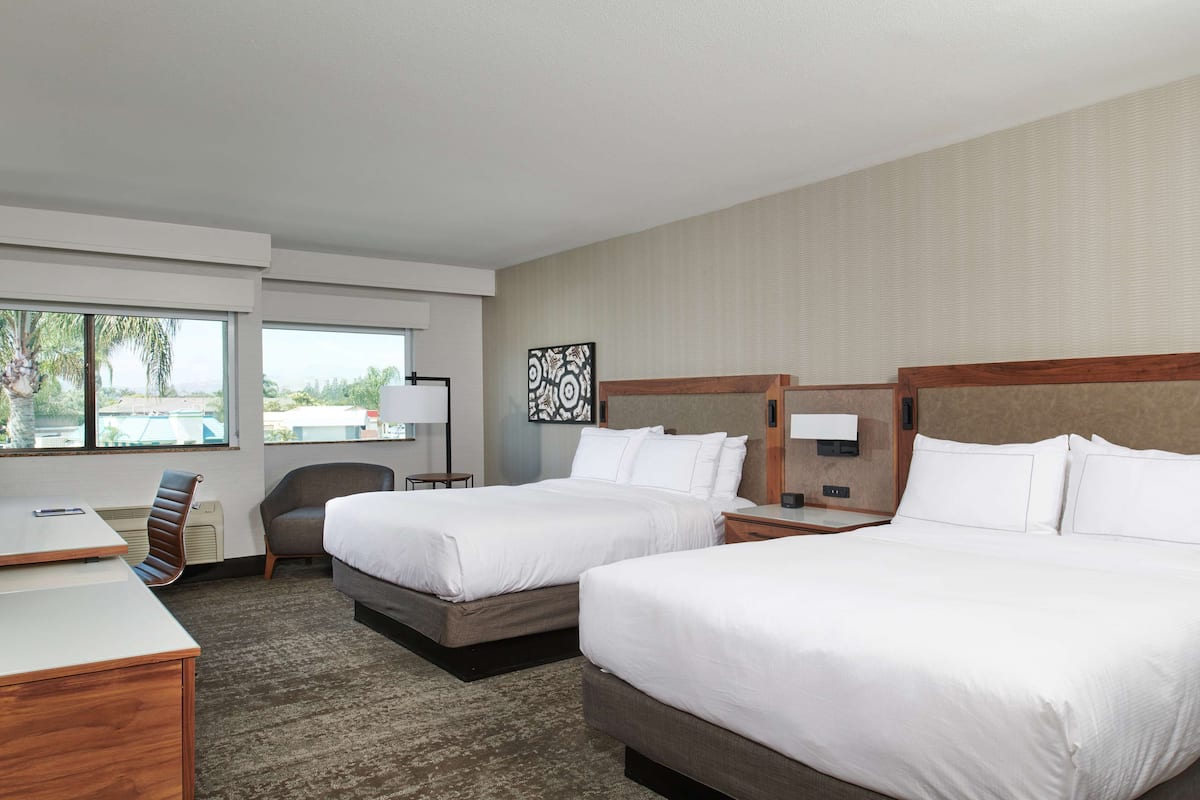 A hotel room with two beds, a desk, a chair, and a large window.