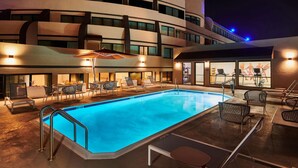 A swimming pool area with lounge chairs and umbrellas, surrounded by a modern building with multiple floors and balconies. - DoubleTree by Hilton Fullerton (Fullerton)