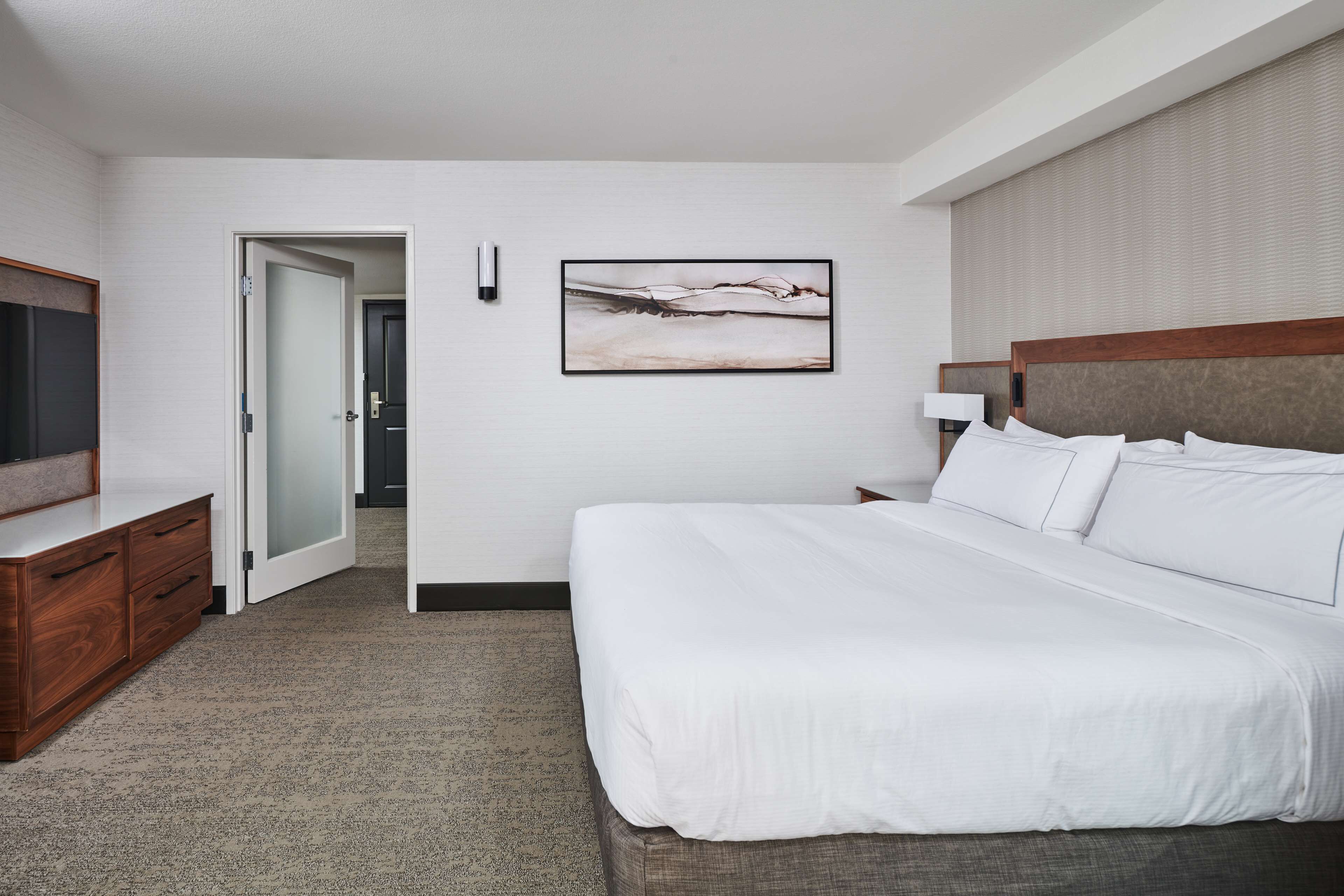 A hotel room with a large bed, a flat-screen TV, a wooden dresser, and a painting on the wall.