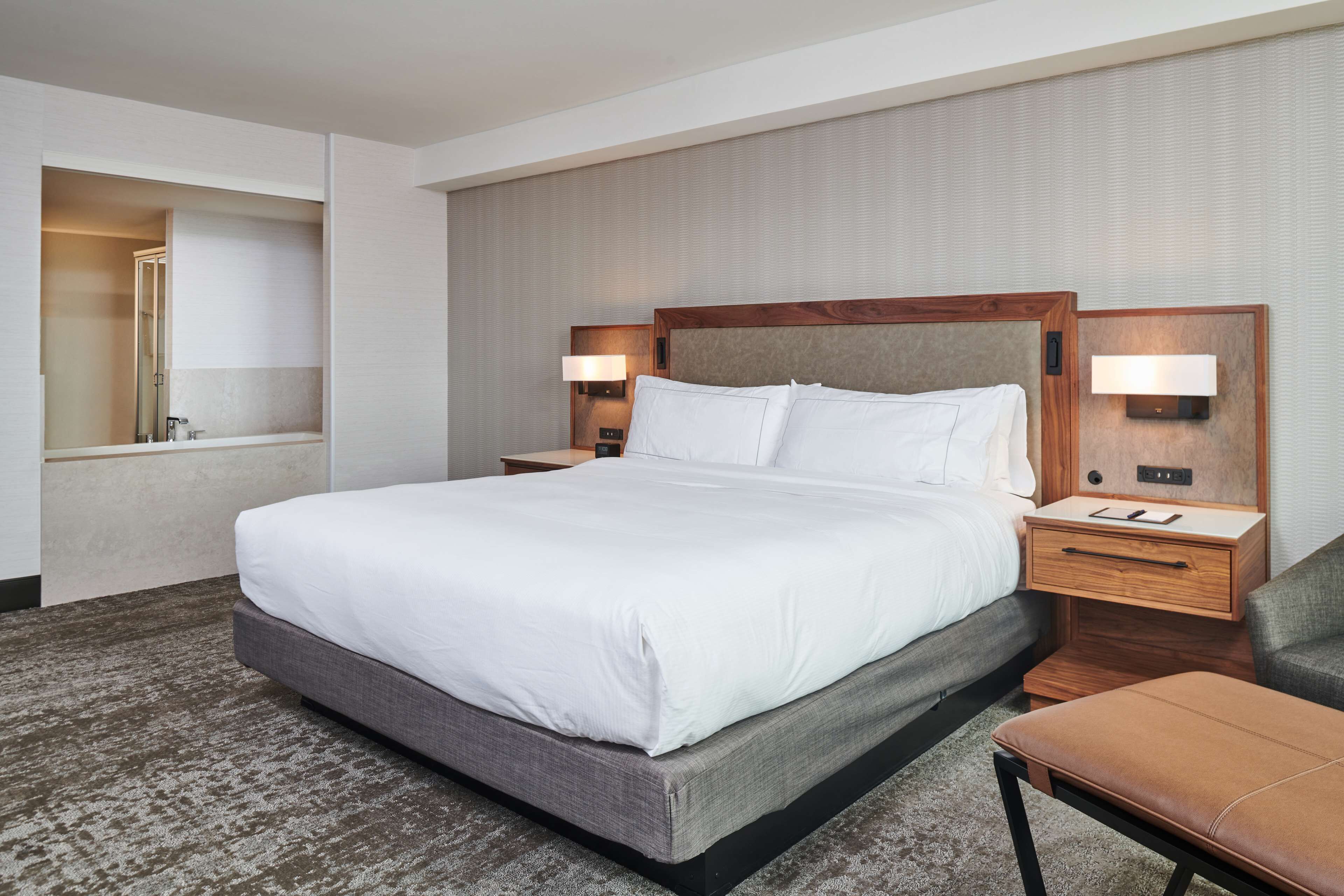 A hotel room with a large bed, bedside tables, a nightstand, a chair, and a mirror.