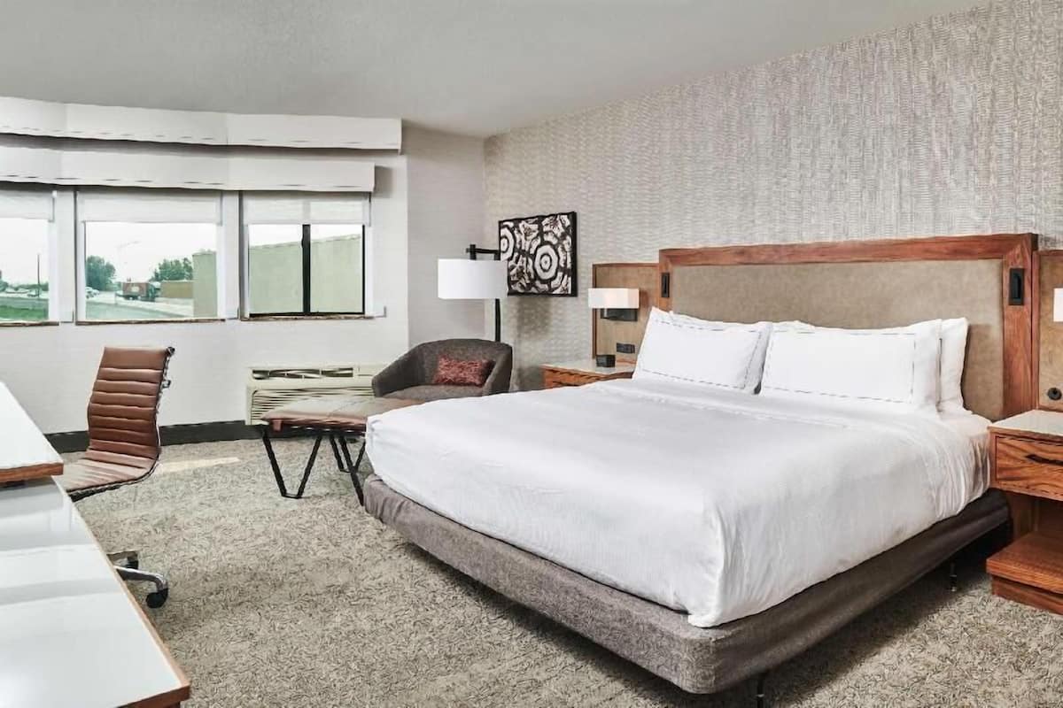 A hotel room with a large bed, a desk, a chair, a lamp, and a window with a view.