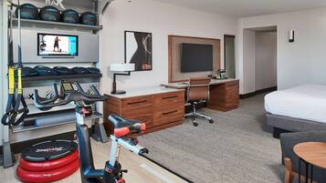 A hotel room with a treadmill, exercise balls, a TV, a desk, a chair, a bed, and a small table.