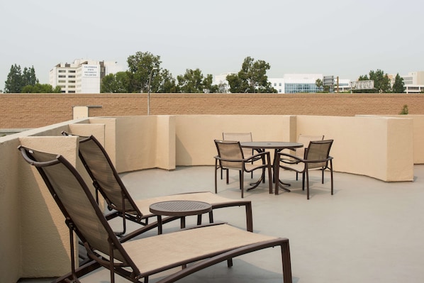 An outdoor seating area with cushioned chairs and a table, surrounded by a low brick wall.