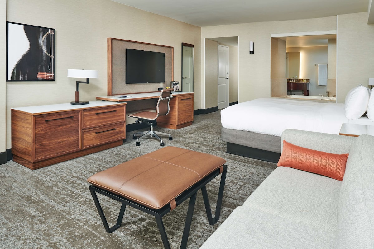A hotel room with a bed, a desk, a chair, a small table, and a sofa.