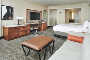 Quarto de hotel com cama, escrivaninha, cadeira, mesa pequena e sofá.