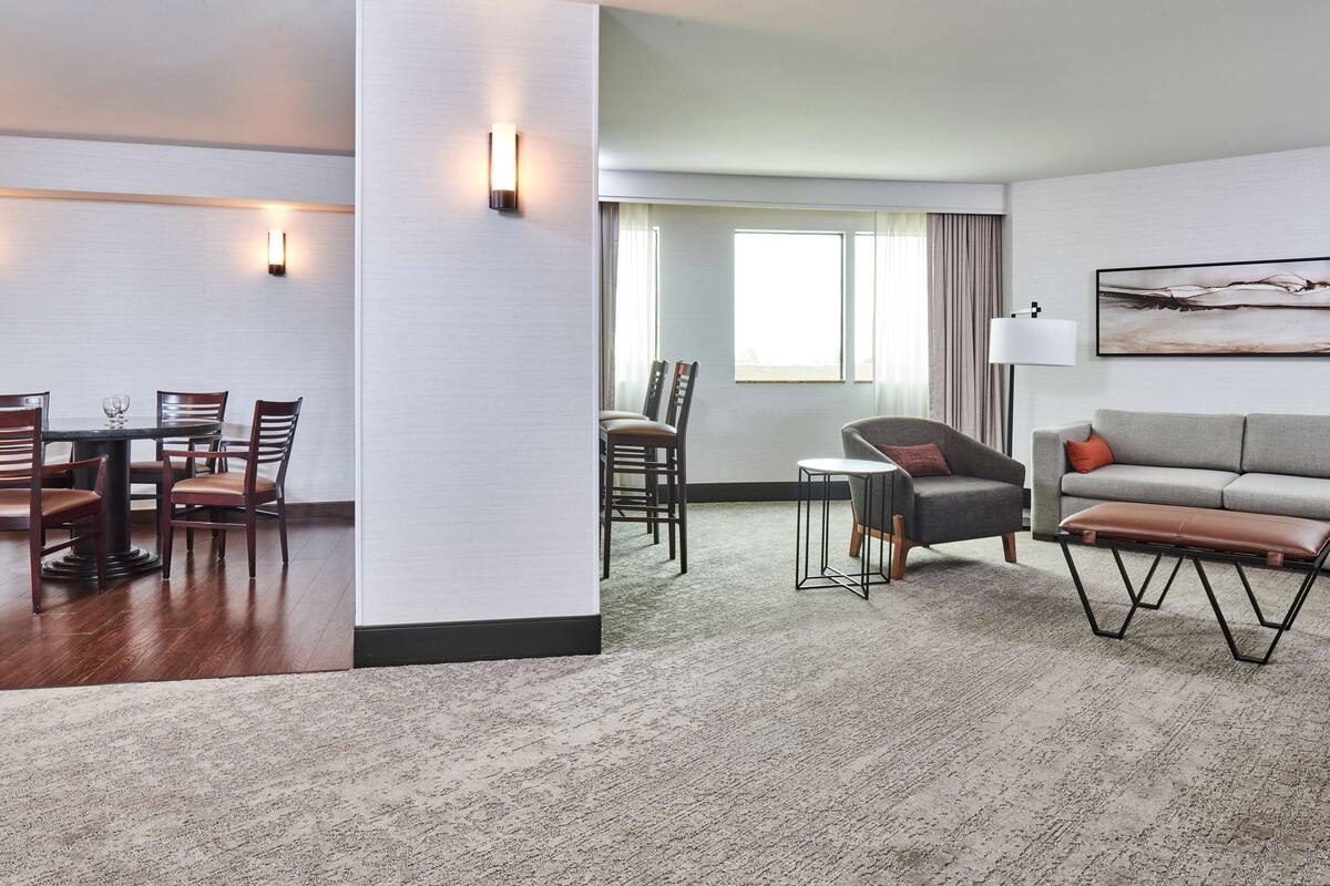 A modern hotel room with a dining area, a sofa, and a bench.