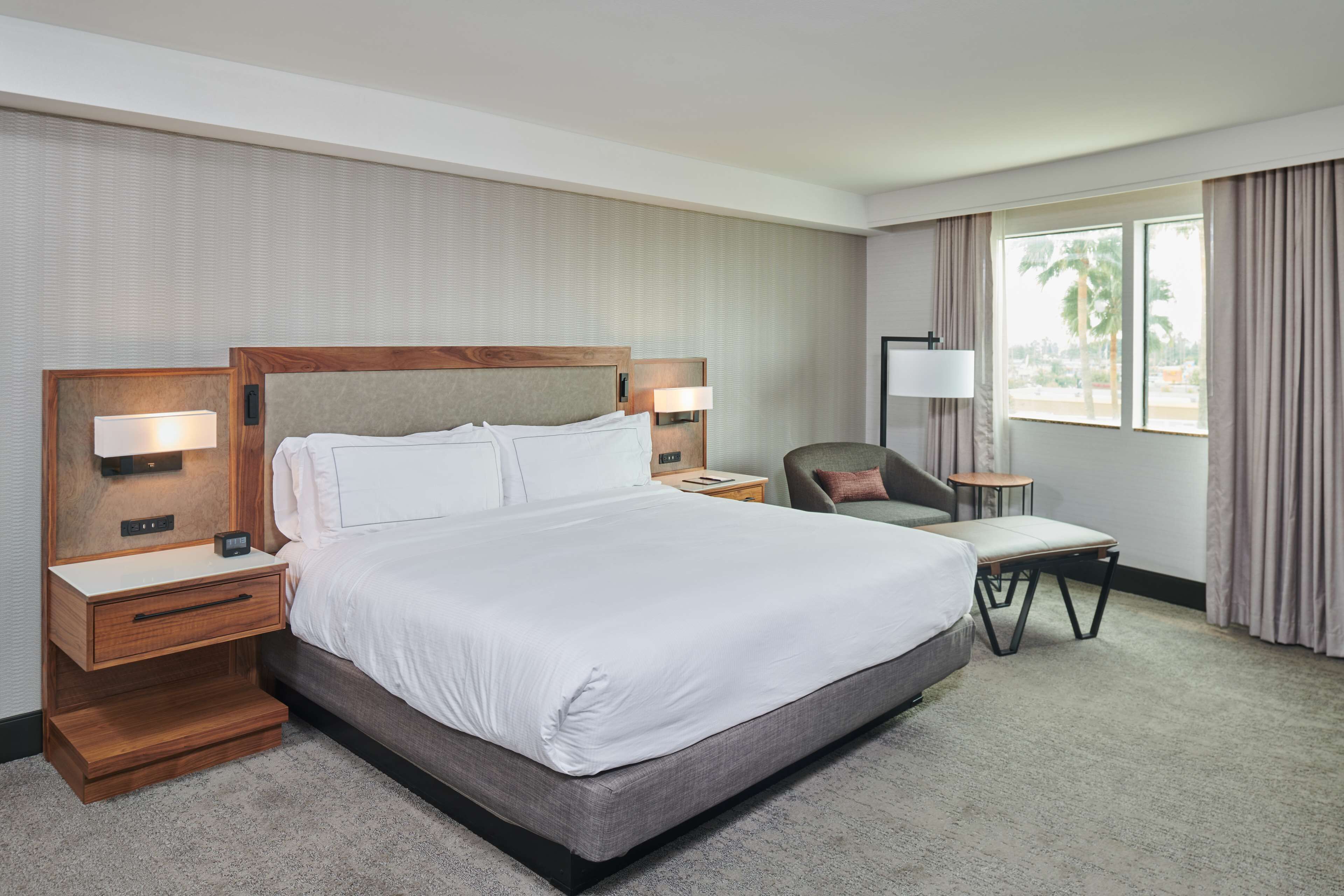 A hotel room with a large bed, bedside tables with lamps, a small desk, and a chair.