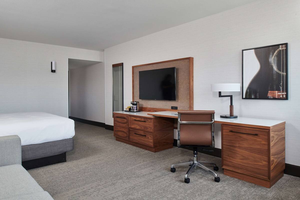 A hotel room with a bed, a wooden desk, a chair, a television, and a lamp.