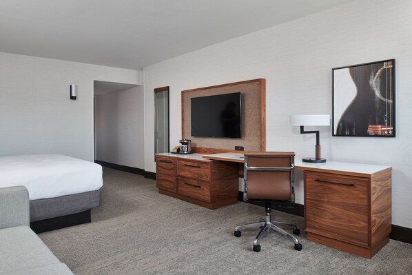 A hotel room with a bed, a wooden desk, a chair, a television, and a lamp.
