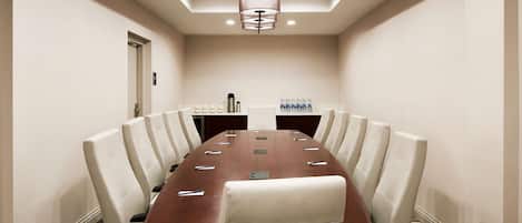A conference room with a long table, white leather chairs, and a ceiling light fixture.