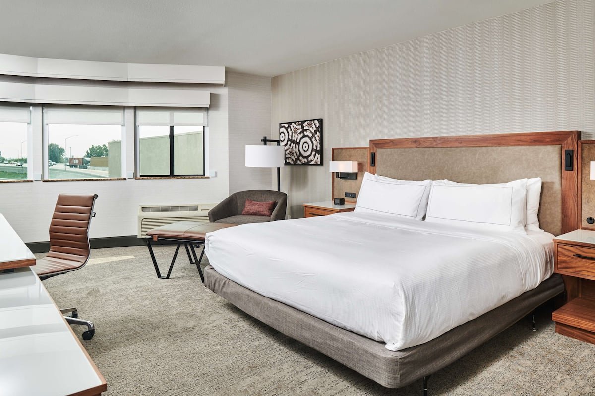 A hotel room with a large bed, a desk, a chair, a lamp, and a window with a view of the outside.