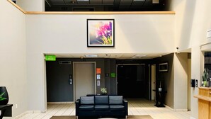 Un hall d’entrée spacieux avec un canapé noir, une table basse ronde et des fauteuils gris. Un comptoir d’accueil se trouve à droite, ainsi qu’un panneau indiquant l’emplacement de la piscine et du jacuzzi.