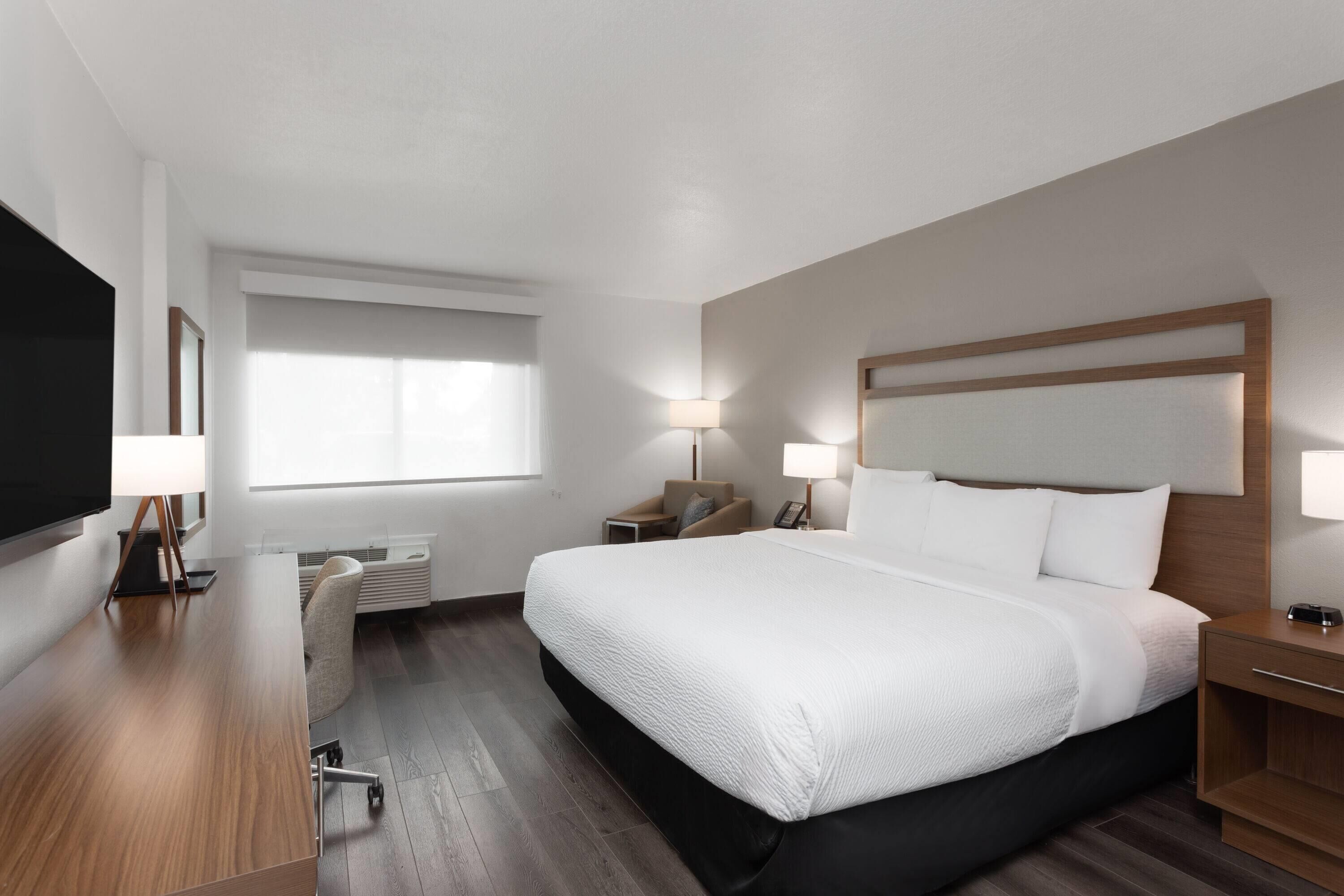A hotel room with a large bed, bedside tables, a desk, and a flat-screen TV.