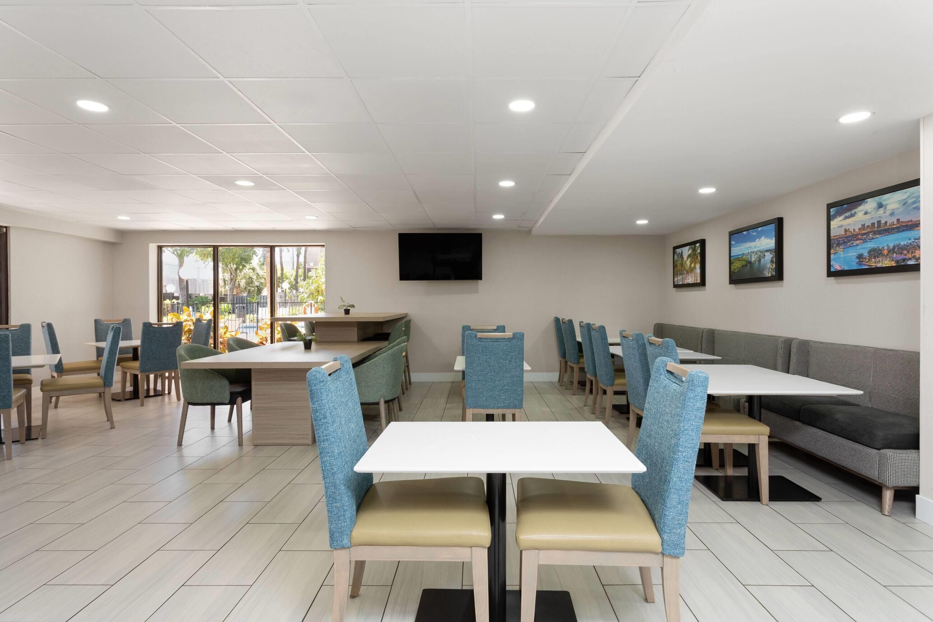 Un comedor moderno con mesas y sillas, un televisor de pantalla plana montado en la pared y cuadros enmarcados.