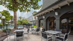 Un espace extérieur aménagé en terrasse, avec des tables et des chaises, une piscine et un bâtiment doté d’arches et de colonnes.