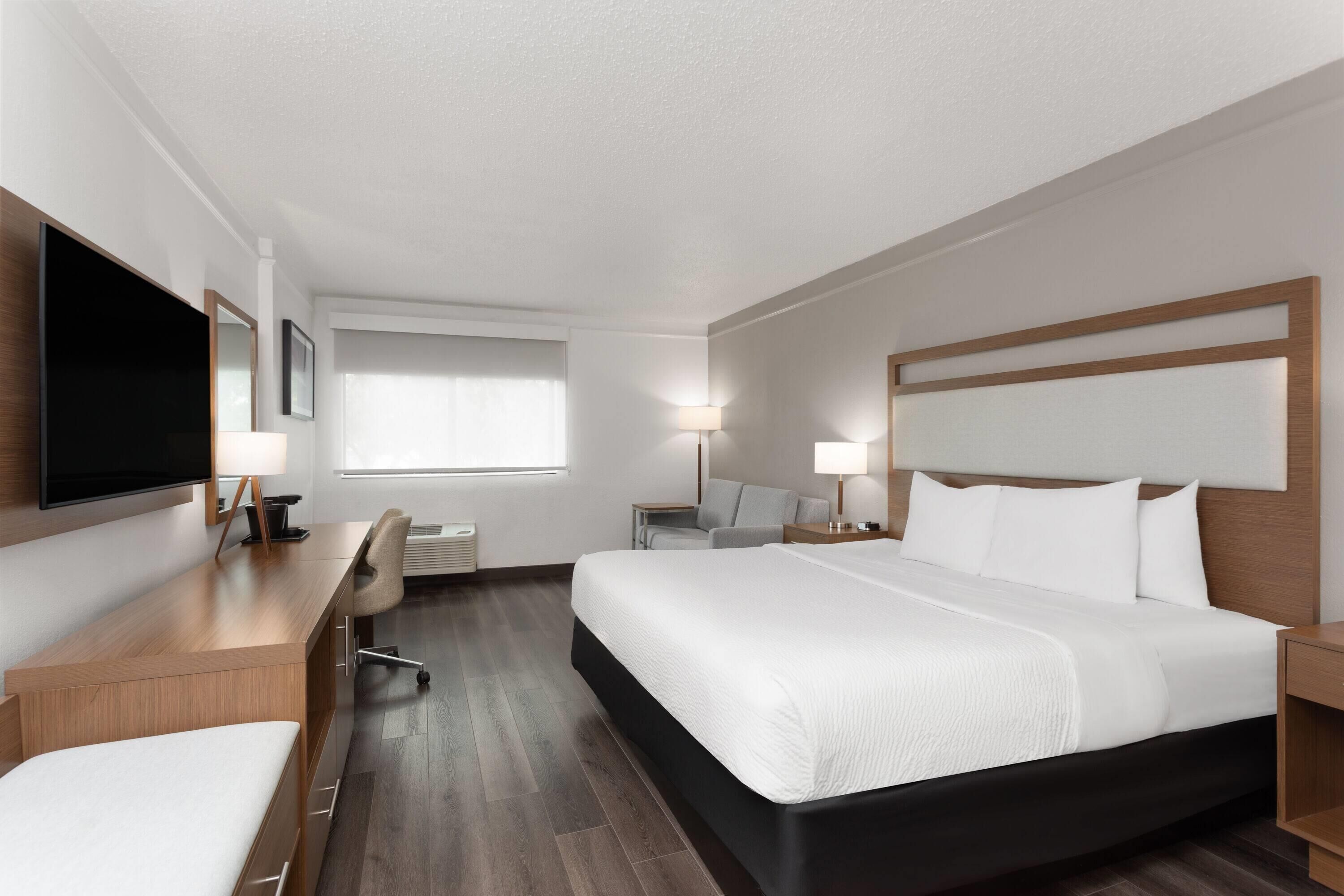 A hotel room with a large bed, a desk with a chair, a TV, and a window with curtains.