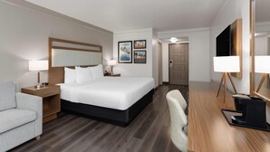 Une chambre d’hôtel avec un grand lit, des tables de chevet, un bureau, une chaise, une télévision et des œuvres d’art accrochées aux murs.