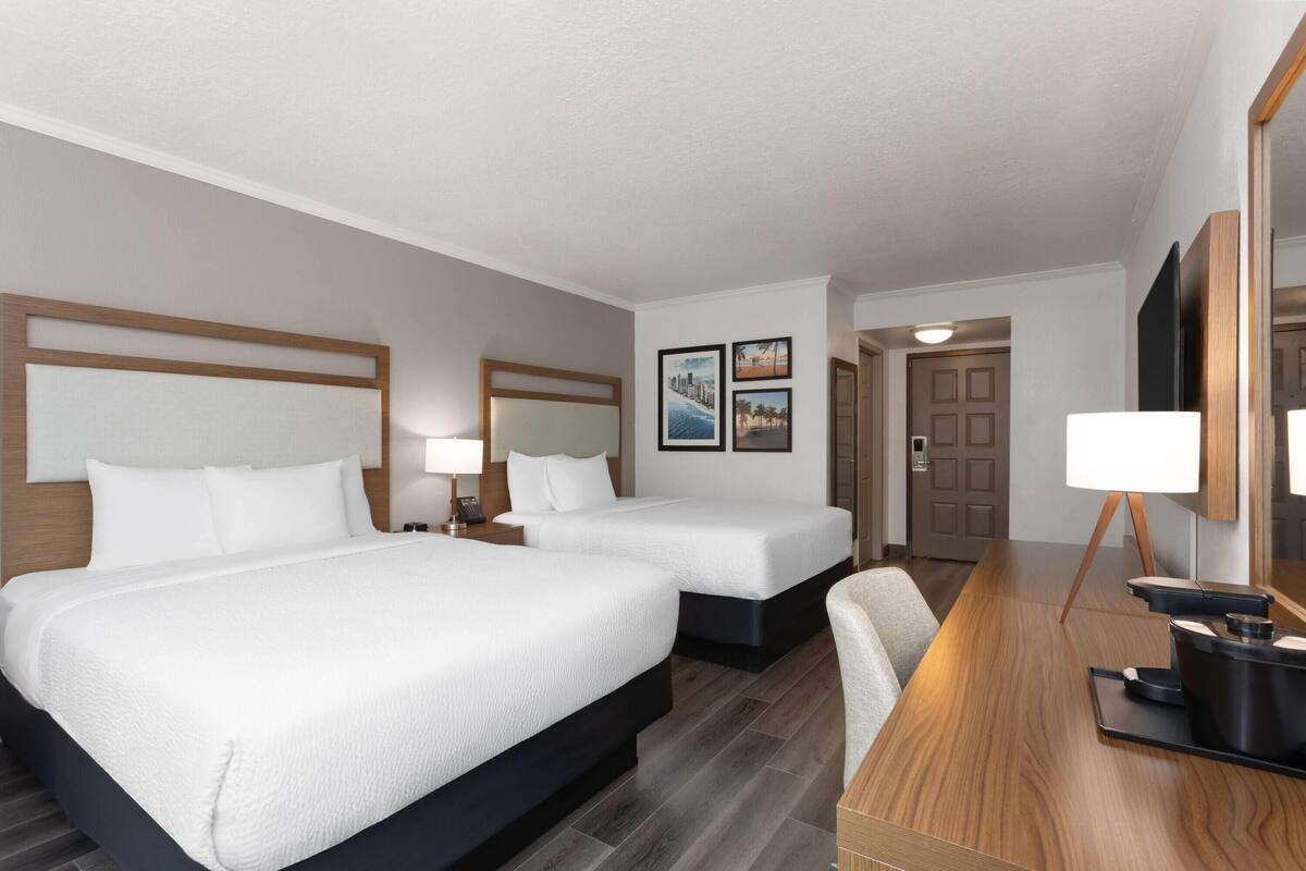 A hotel room with two beds, a desk with a lamp, and a large mirror.