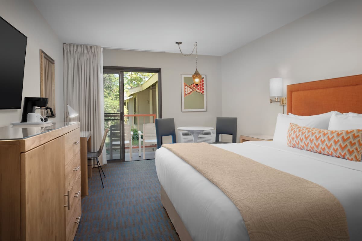 A hotel room with a bed, a desk, a chair, a coffee maker, and a view of the outdoors.